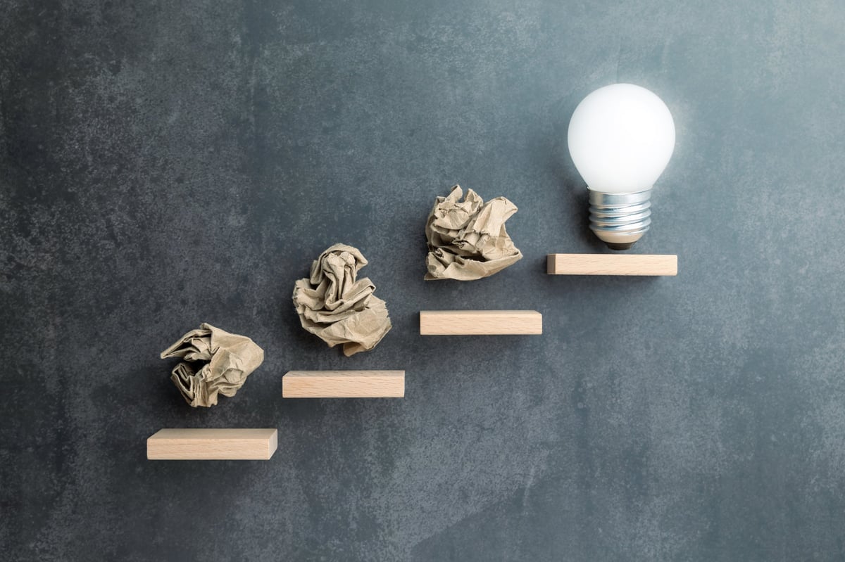 Steps leading up to a glowing light bulb, symbolizing how effort and learning lead to a breakthrough
