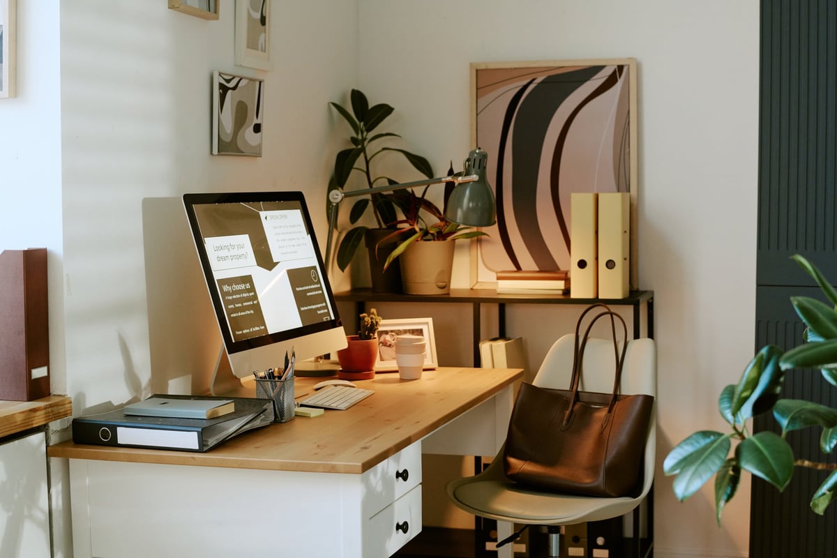 A modern home office desk with a computer showing charts and documents, notebooks and plants